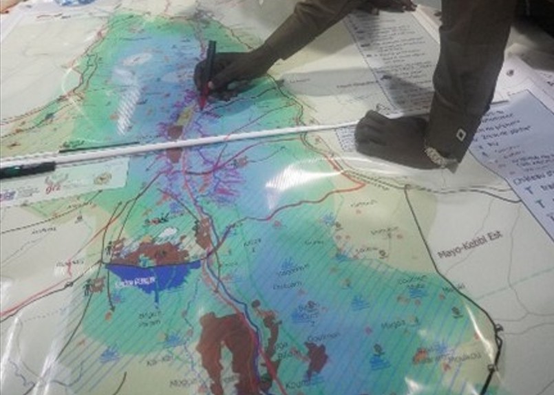 A big map on a table and hands tracing the map with pen and ruler.