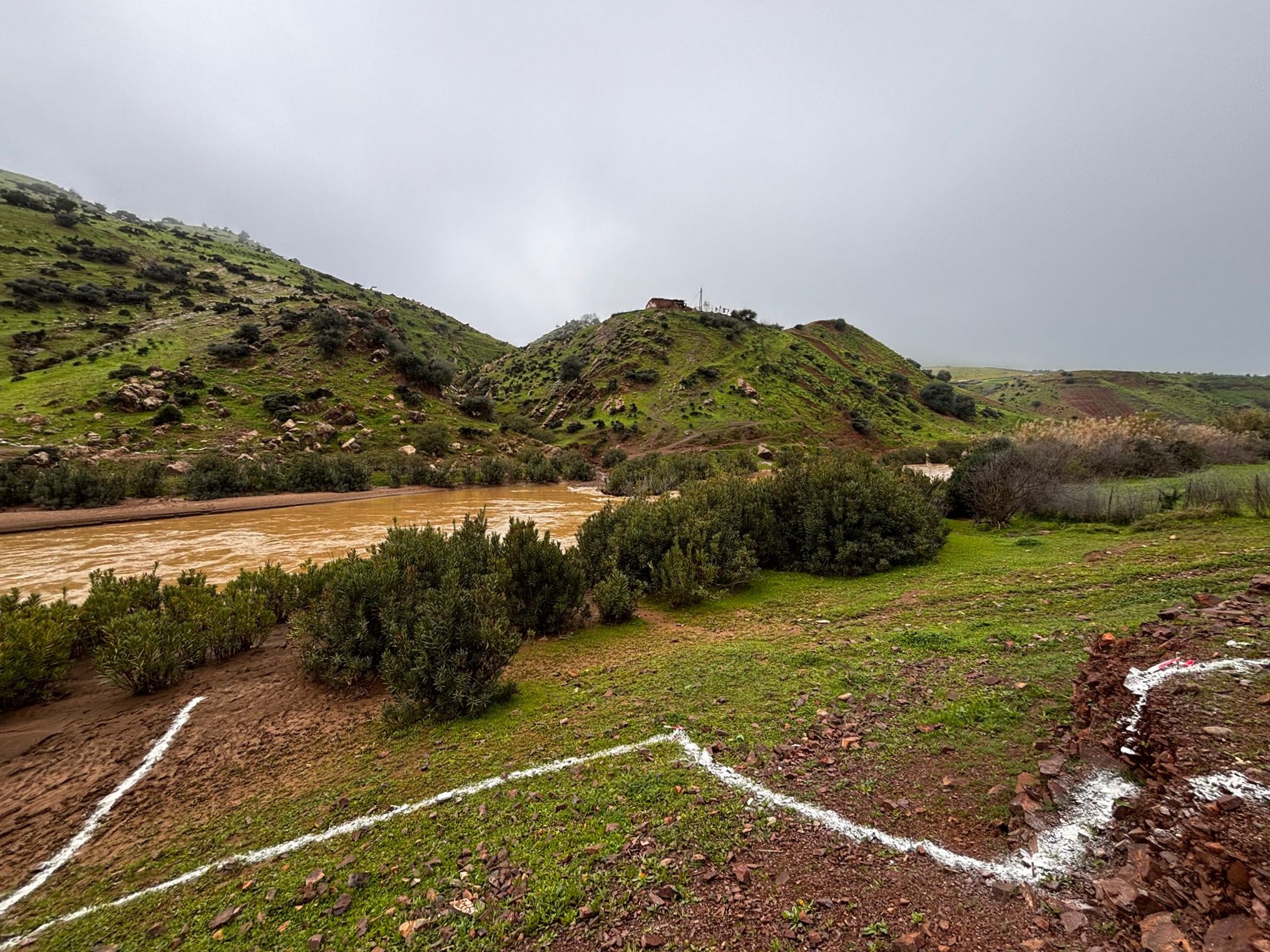 Demarcations on a field next to a river under a grey, cloudy sky.