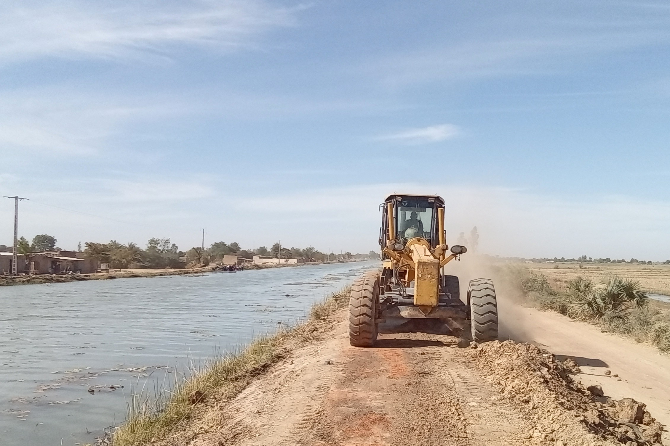 A tractor drives along the bank of a distribution canal.
