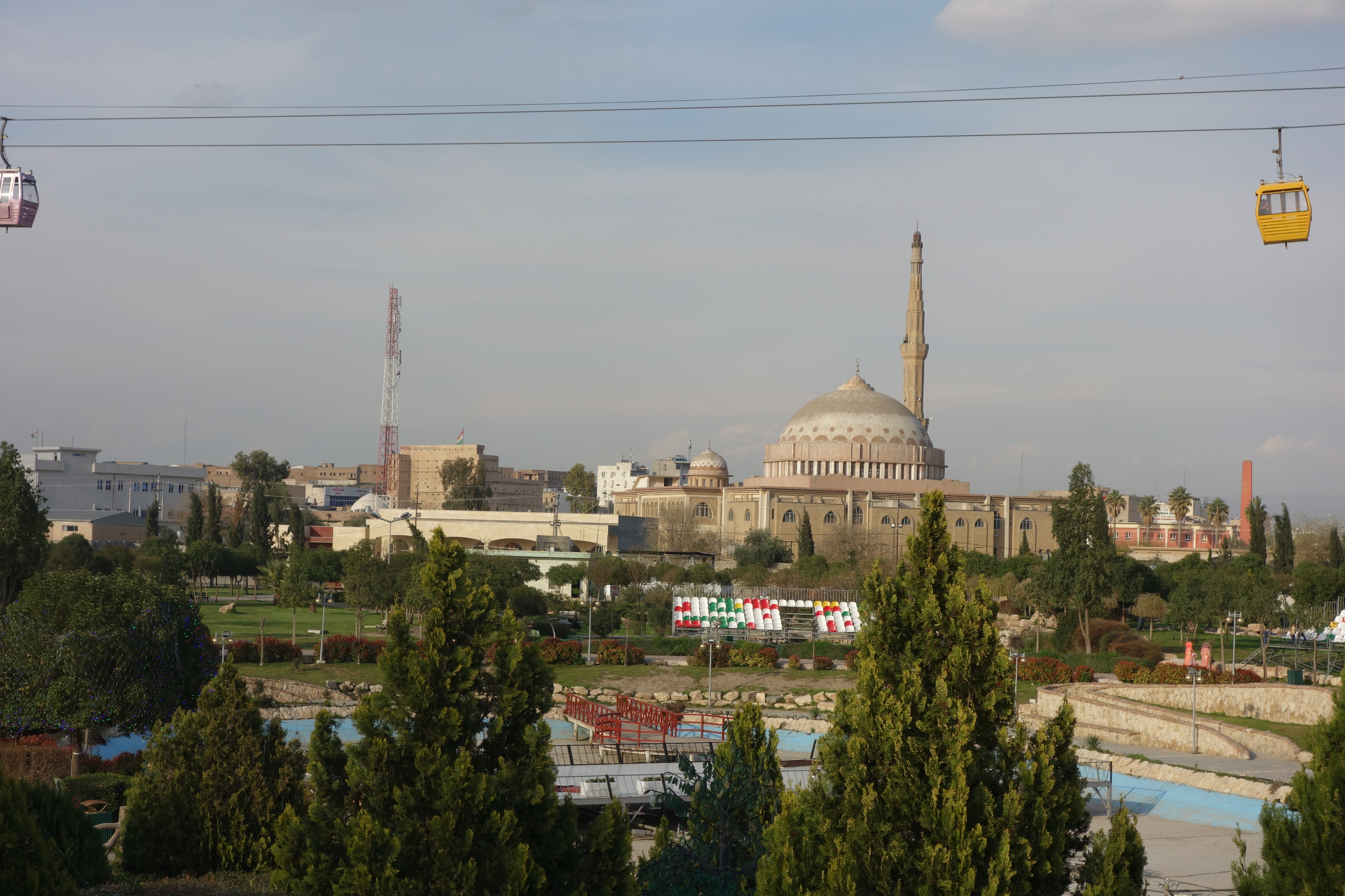 View of a city with a park in the front, a cable car, and a mosque in the back.