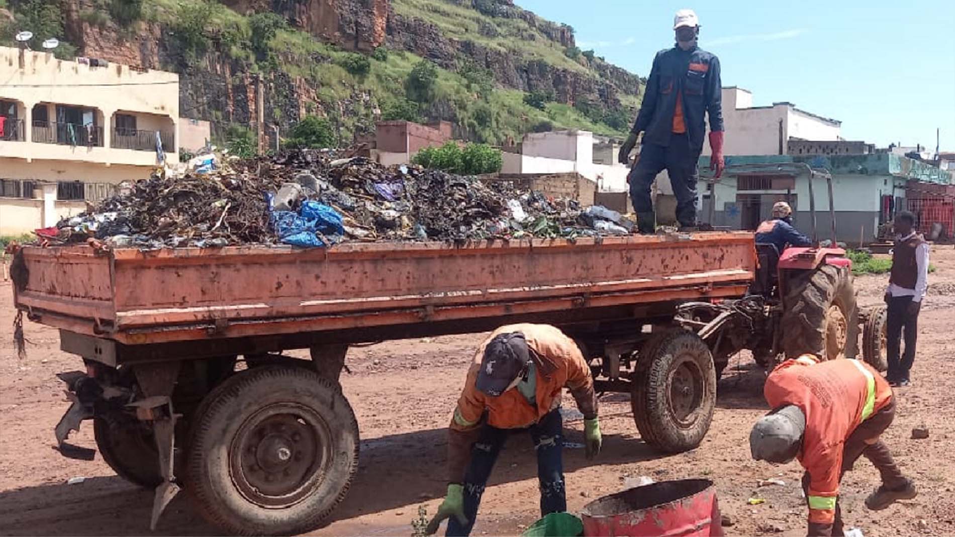 Waste collectors with trailer and tractor working on the street.
