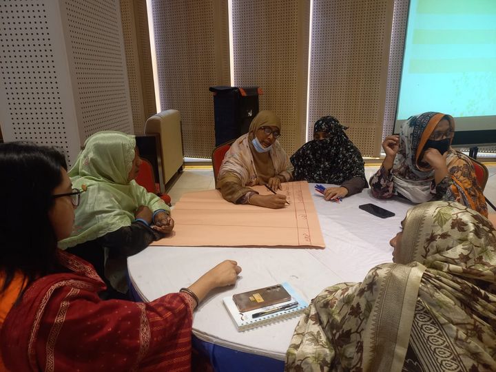 A group of women of which some with headscarves sitting around a table discussing and noting down things.