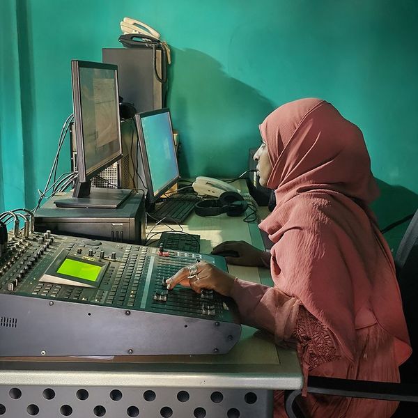 An Ethiopian woman with a traditional head scarf is sitting at a mix table in a radio studio.