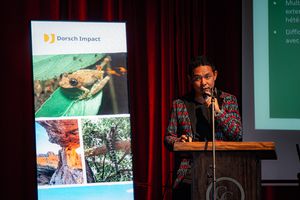 A man in a colourful blazer speaking into a microphone behind a podest.