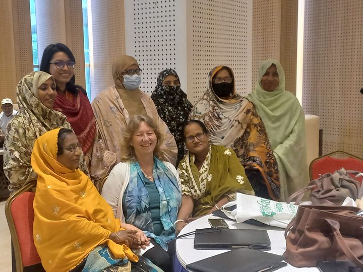 A group of nine smiling women posing around a round table for a photograph.
