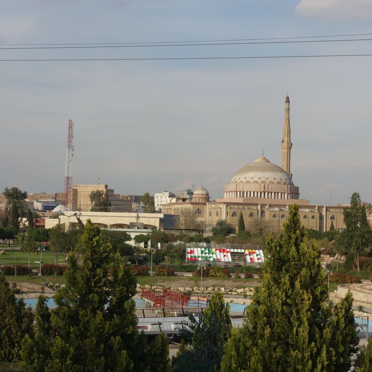 View of a city with a park in the front, a cable car, and a mosque in the back.