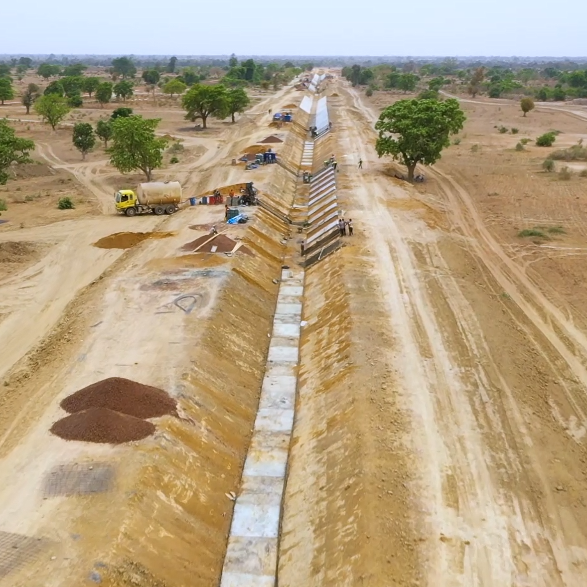 In the middle of a wide arid landscape with a few trees a trench in construction for the northern extension of the Tiékélinso North Perimeter in the San-Ouest Plain, Mali.
