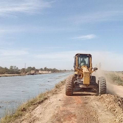 A tractor drives along the bank of a distribution canal.