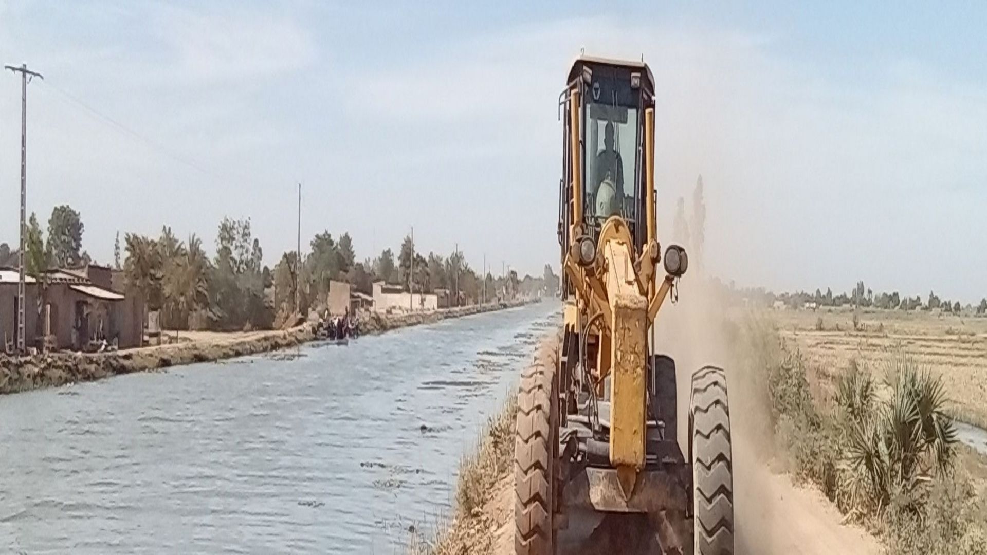 A tractor drives along the bank of a distribution canal.