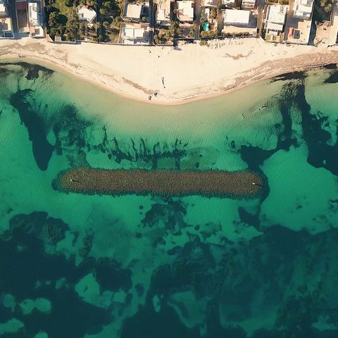 Bird view a coastal city at a white beach and the transparent turquoise sea with a breakwater to protect the coastal zone..
