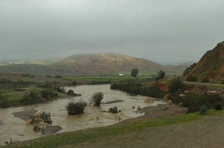 A river course between hills under a grey, cloudy sky.