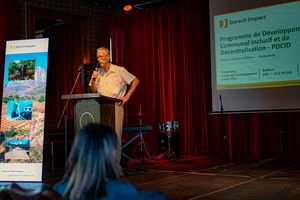 A tall man standing at a podest infront of a screen.