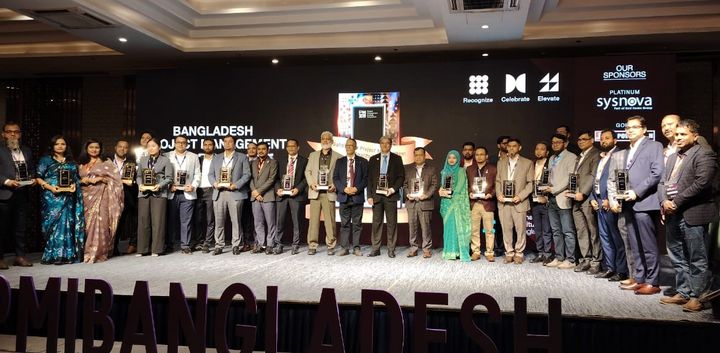 A large group of people with their respective awards standing next to another behind a sign saying #pmibangladesh.