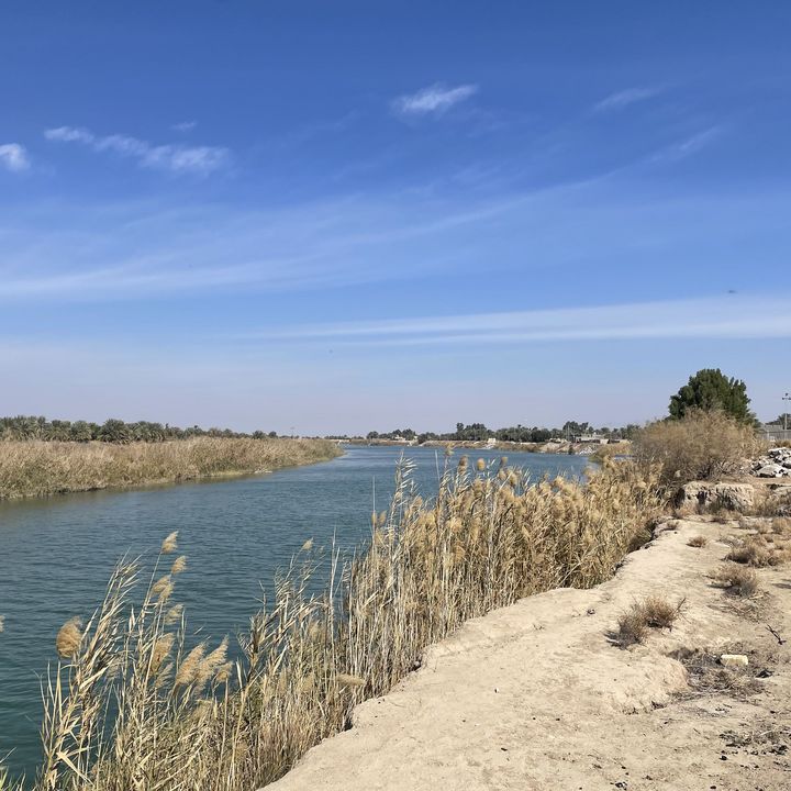 A blue sky above a calm canal between sandy banks.