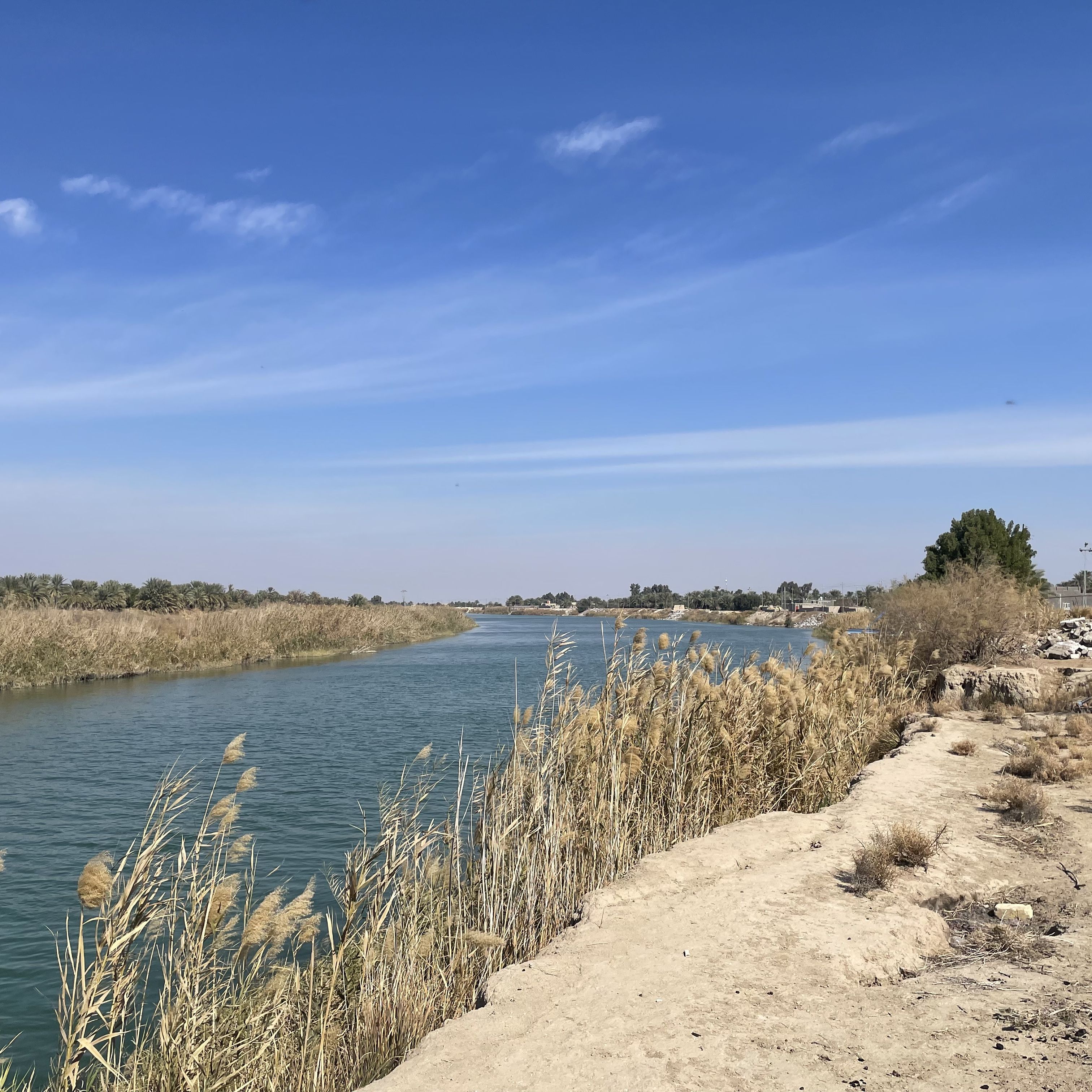 A blue sky above a calm canal between sandy banks.