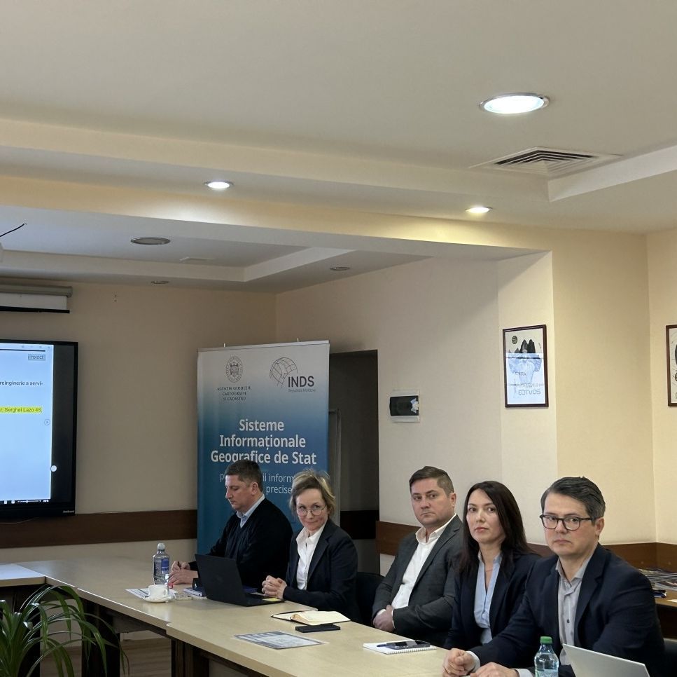 Five people in business clothing sitting at a long table in a conference room with a presentation projected at the back wall.