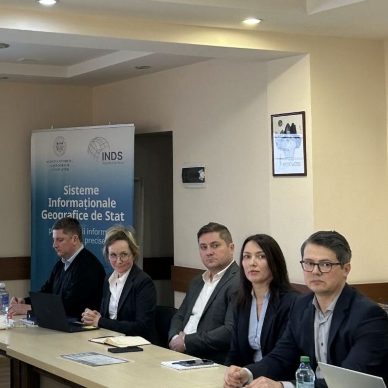 Five people in business clothing sitting at a long table in a conference room with a presentation projected at the back wall.
